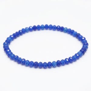 May include: A circular bracelet composed of numerous small, faceted, deep blue beads. The beads are uniform in size and shape, creating a continuous, reflective, and textured surface throughout the entire length of the circular jewellery piece.