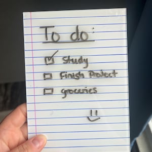 May include: A clear, rectangular to-do list with blue horizontal lines and the words "To do:" at the top. The list includes "Study," "Finish Project," and "groceries," with a checkmark next to "Study." A smiley face is drawn at the bottom.