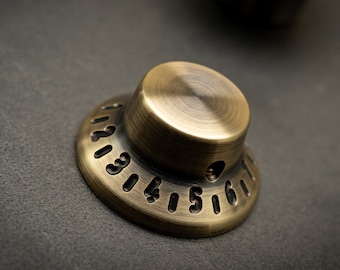 May include: A brass knob with a circular base and a raised top. The base has numbers 1 through 6 engraved around the edge.