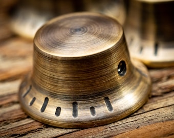 May include: A close-up of a gold-toned metal knob with a textured surface and a black ring around the edge. The knob has a small hole in the centre.