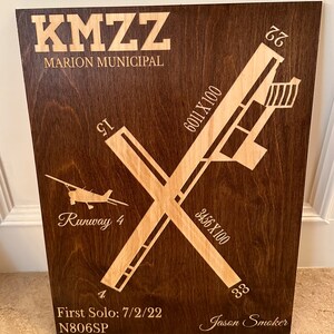 K&ouml;nnte beinhalten: Eine Holzplakette mit braunem Hintergrund und einem hellbraunen Landebahn-Design. Die Plakette tr&auml;gt den Text "KMZZ MARION MUNICIPAL" oben, "Runway 4" in der Mitte und "First Solo: 7/2/22 N806SP" unten. Die Plakette enth&auml;lt auch den Text "Jason Smoker" und die Zahlen "6011 X 100", "3456 X 100", "77", "GI", "4" und "33".
