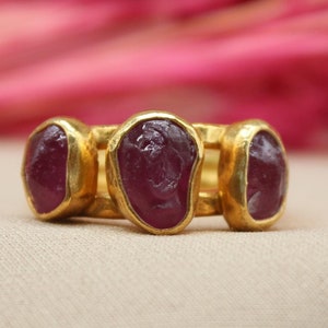 May include: A gold ring with three ruby stones set in the band. The stones are a deep red color and have a slightly irregular shape.