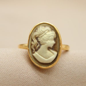 May include: A gold ring with a cameo featuring a woman's profile in white.