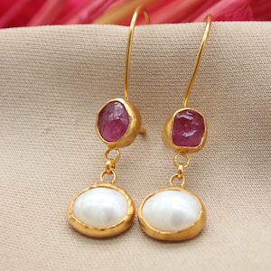 Pode incluir: Brincos de ouro com uma gema rosa e uma pérola branca.