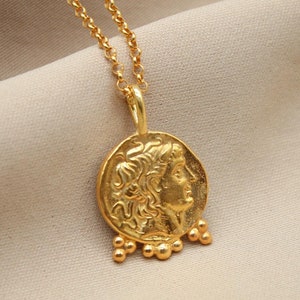 May include: A gold necklace with a coin pendant featuring a profile of a person's face. The pendant has small gold beads hanging from the bottom.
