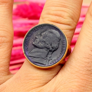 Op de afbeelding: Een gouden ring met een zwart, gedetailleerd beeld van een mannenprofiel. De ring heeft de inscripties "In God We Trust" en "Liberty 1943".