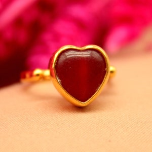 Könnte beinhalten: Ein goldener Ring mit einem roten herzförmigen Stein.