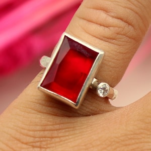 May include: A silver ring featuring a large, rectangular, red gemstone and a smaller, round, clear gemstone.
