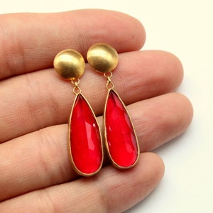 Op de afbeelding: Een paar gouden oorhangers met rode traanvormige glazen stenen.