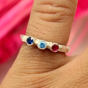 May include: A silver ring with three gemstones: a blue sapphire, a light blue topaz, and a red ruby.