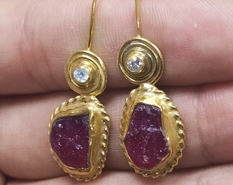 May include: A pair of gold earrings with a red gemstone and a small clear stone accent.