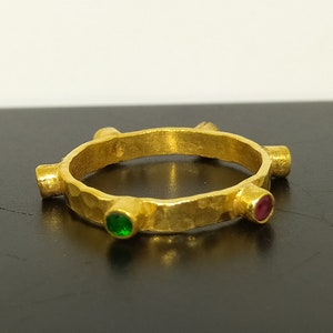May include: A gold ring with five prongs, each prong set with a gemstone. Two of the prongs are set with green gemstones, and three of the prongs are set with red gemstones.
