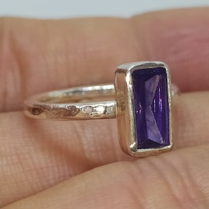 May include: A silver ring featuring a rectangular purple amethyst gemstone. The ring band has a hammered finish.
