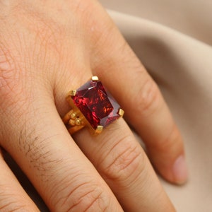 May include: A gold ring with a large, square, red gemstone.