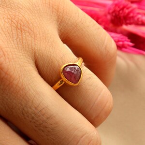 May include: A gold ring with a pink gemstone set in a triangular shape.