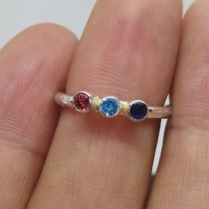 Op de afbeelding: Een zilveren ring met drie kleine edelstenen. De edelstenen zijn roze, blauw en donkerblauw.
