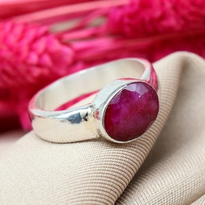 Peut inclure: Une bague en argent avec une grande pierre précieuse de rubis de forme ovale. Le rubis est d'une couleur rouge foncé et riche.