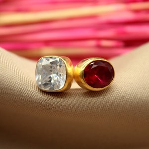May include: A pair of gold earrings with a clear square-shaped stone and a red round stone.
