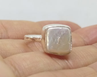 May include: A silver ring with a square-shaped white pearl set in the center.
