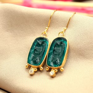 May include: Gold dangle earrings with green glass cameo insets and clear crystal accents.