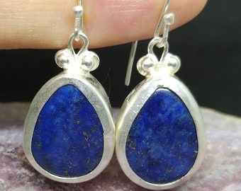 Può includere: Un paio di orecchini a goccia d'argento con pietre di lapislazzuli blu. Gli orecchini hanno un design semplice con una finitura argentata liscia.