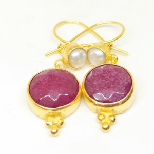 Op de afbeelding: Gouden oorbellen met een roze edelsteen en een parel accent.