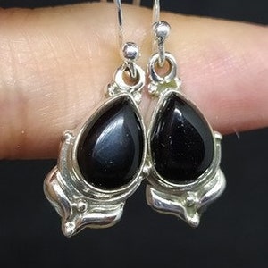 May include: A pair of silver dangle earrings with black teardrop-shaped stones.