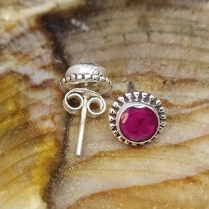 May include: A pair of silver stud earrings with a round, pink gemstone in the centre. The earrings have a beaded border.