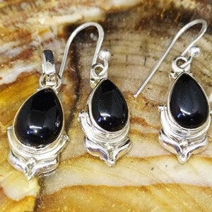 May include: A pair of silver earrings and a pendant featuring black gemstone drops in a teardrop shape. The earrings and pendant have intricate silver designs.