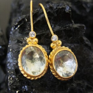 May include: A pair of gold earrings with oval-shaped green gemstones and small clear cubic zirconia accents.