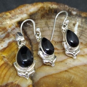 May include: A set of silver earrings and a pendant featuring black gemstone drops. The earrings are teardrop shaped with a delicate floral design. The pendant is similar in style, with a slightly larger gemstone.