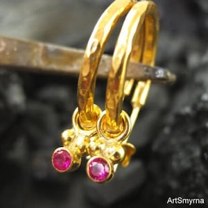 May include: Gold hoop earrings with a hammered texture and small pink gemstones hanging from the bottom.