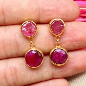 Op de afbeelding: Een paar gouden oorbellen met twee roze edelstenen aan elke oorbel. De oorbellen hangen en de edelstenen zijn gefacetteerd.