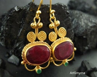 May include: Gold earrings with a red gemstone and green accents. The earrings have a delicate, intricate design.
