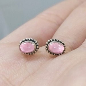 Op de afbeelding: Een paar zilveren oorbellen met roze ovale stenen gezet in een zilveren bezel.