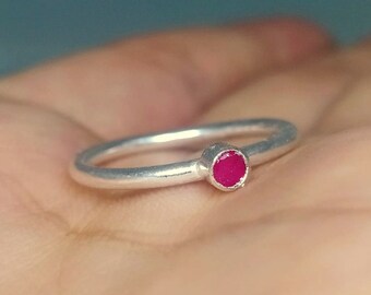 Op de afbeelding: Een zilveren ring met een kleine, felroze edelsteen.