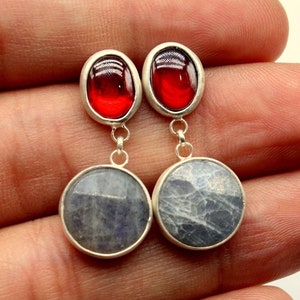 May include: A pair of silver dangle earrings with red oval-shaped stones and round blue stones.