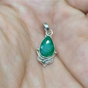 Pu&ograve; includere: Un ciondolo a forma di goccia con una vibrante pietra preziosa verde incastonata in metallo color argento. La pietra preziosa ha molteplici sfaccettature e l'incastonatura in metallo ha un design decorativo.