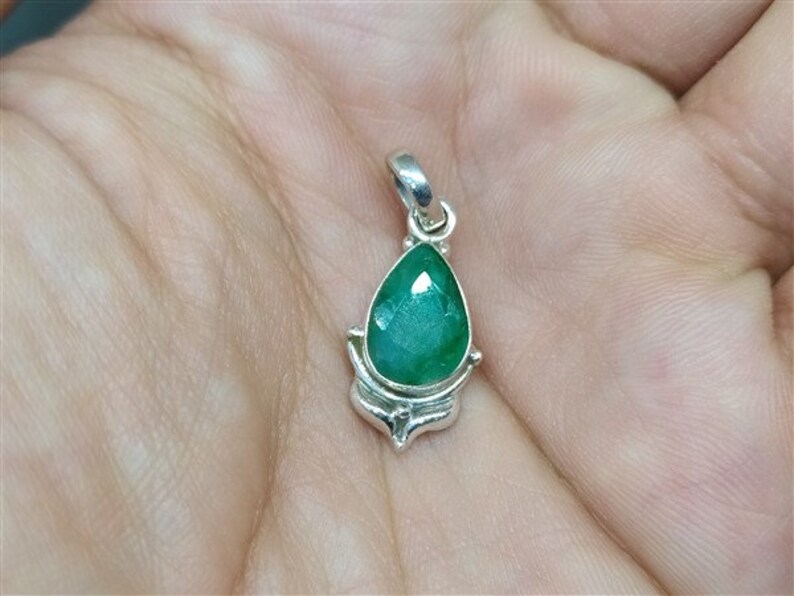 Pu&ograve; includere: Un ciondolo a forma di goccia con una vibrante pietra preziosa verde incastonata in metallo color argento. La pietra preziosa ha molteplici sfaccettature e l'incastonatura in metallo ha un design decorativo.