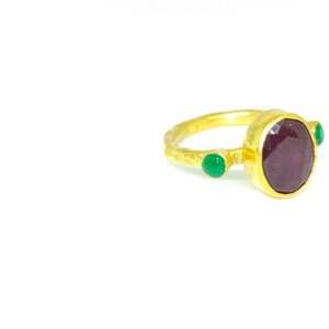 May include: A gold ring featuring a large oval ruby gemstone and two smaller green gemstones.
