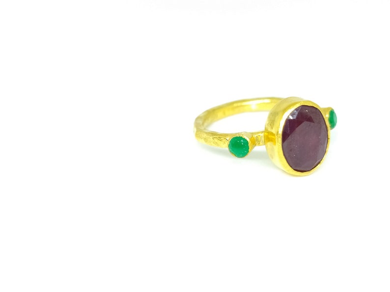 May include: A gold ring featuring a large oval ruby gemstone and two smaller green gemstones.