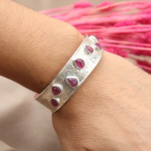 May include: A silver bangle bracelet with a hammered texture and pink gemstones set into the metal.