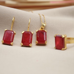 May include: A gold jewelry set with red gemstone earrings, a pendant necklace, and a ring. The gemstones are emerald cut and have a deep red color.
