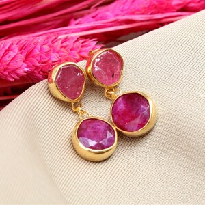 Op de afbeelding: Gouden oorbellen met roze edelsteen druppels. De oorbellen hebben twee ronde roze edelstenen en twee kleinere, onregelmatig gevormde roze edelstenen.