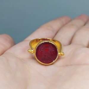 Peut inclure: Une bague en or avec une pierre pr&eacute;cieuse rouge sertie dans un sertissage &agrave; b&eacute;li&egrave;re. La bague a un design pivotant, permettant &agrave; la pierre pr&eacute;cieuse de tourner.