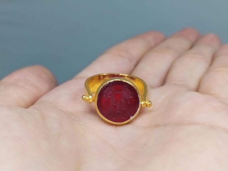 Peut inclure: Une bague en or avec une pierre pr&eacute;cieuse rouge sertie dans un sertissage &agrave; b&eacute;li&egrave;re. La bague a un design pivotant, permettant &agrave; la pierre pr&eacute;cieuse de tourner.