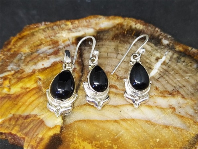 May include: A pair of silver earrings and a pendant featuring black gemstone drops in a teardrop shape. The earrings and pendant have intricate silver designs.