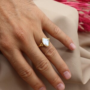 May include: A gold ring with a large, white, triangular gemstone. The ring is on a person's finger.