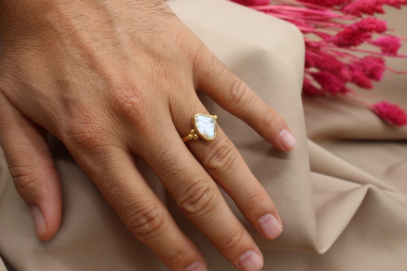 May include: A gold ring with a large, white, triangular gemstone. The ring is on a person's finger.