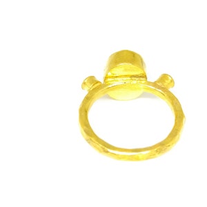 May include: A gold ring with a round, smooth stone set in the centre. The ring has a textured band and is made of hammered metal.